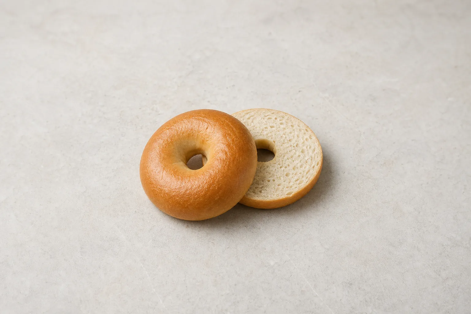 A whole plain bagel and one cut half showing its soft pale crumb.