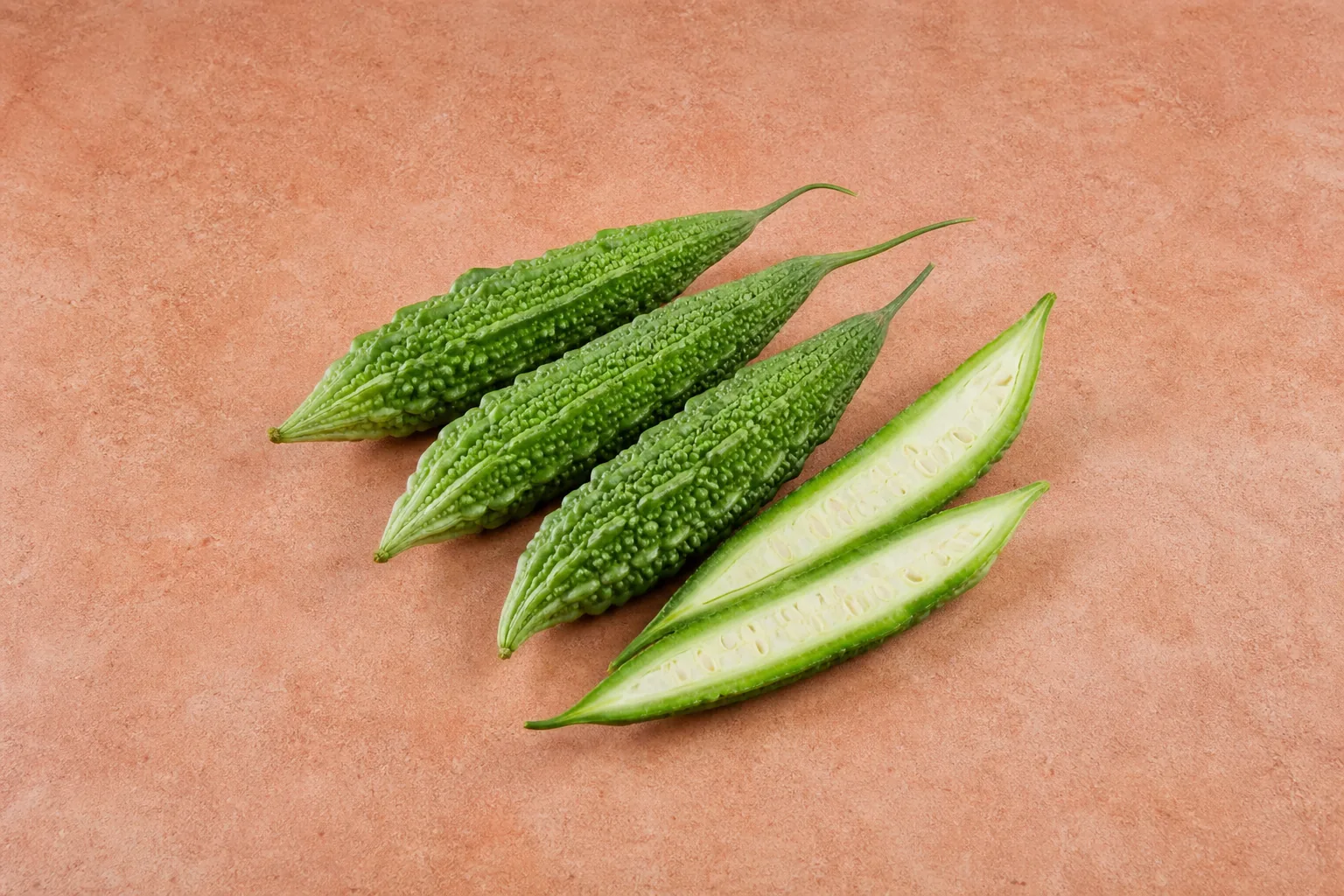 Green ridged bitter melons with one cut open to show its pale interior and seeds.