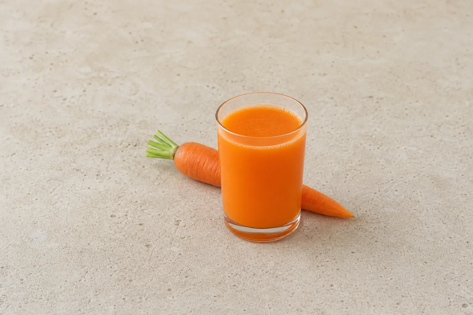 A clear glass of vivid orange carrot juice with one whole carrot behind it.