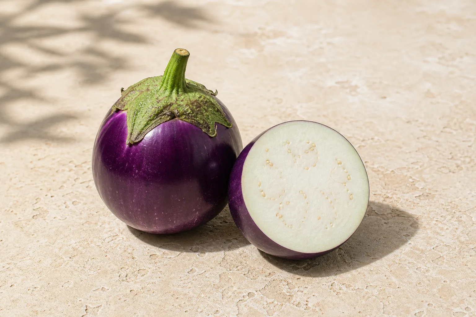 A whole raw purple globe eggplant and one cut half showing pale seeded flesh.