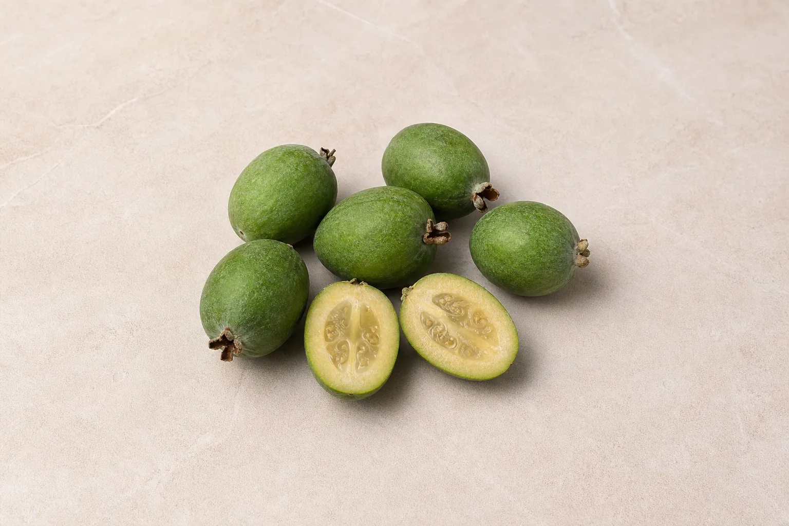 Small oval green raw feijoas with one cut open to show pale flesh and a translucent seed centre.