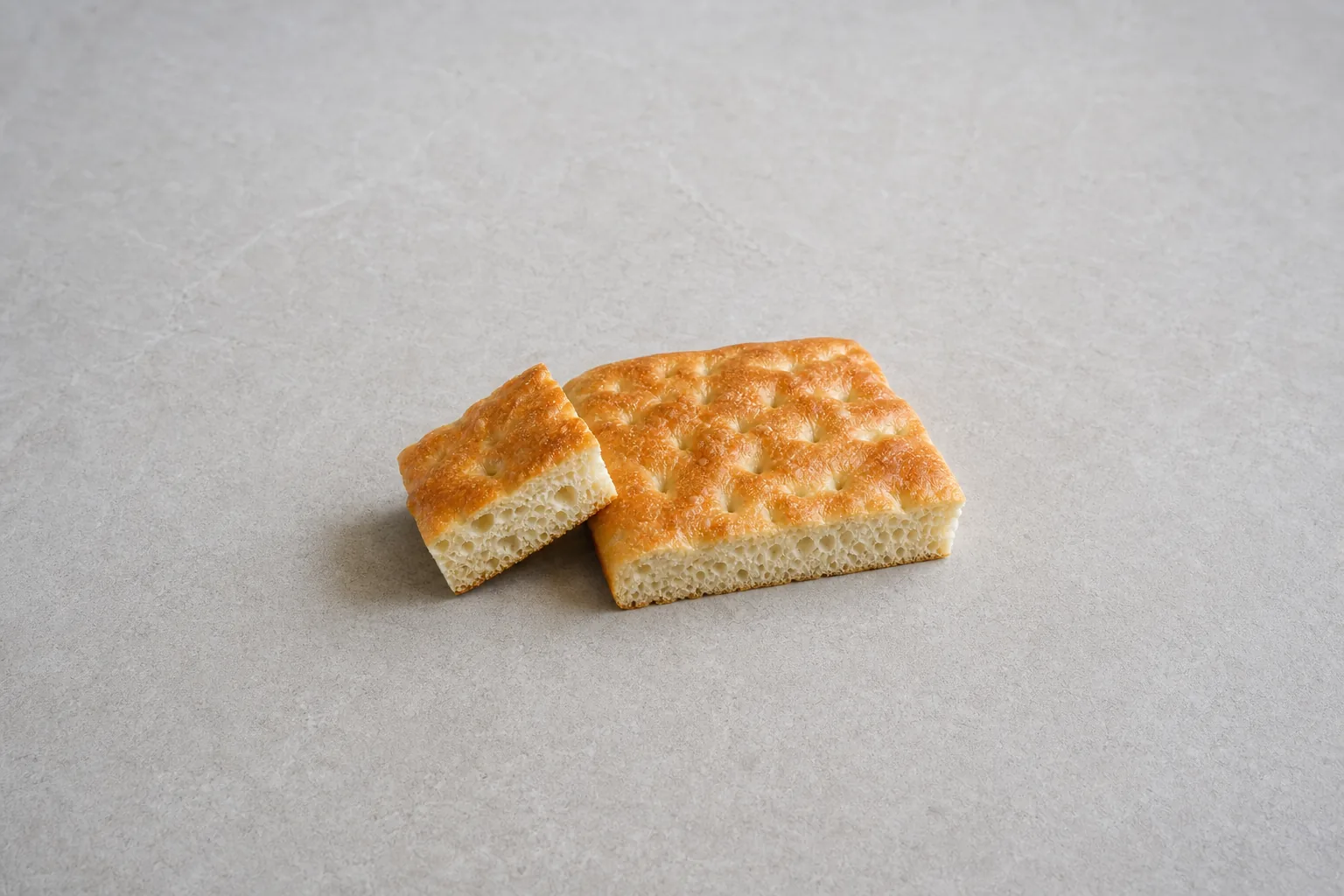 A plain golden slab of dimpled focaccia with one cut square showing its airy crumb.
