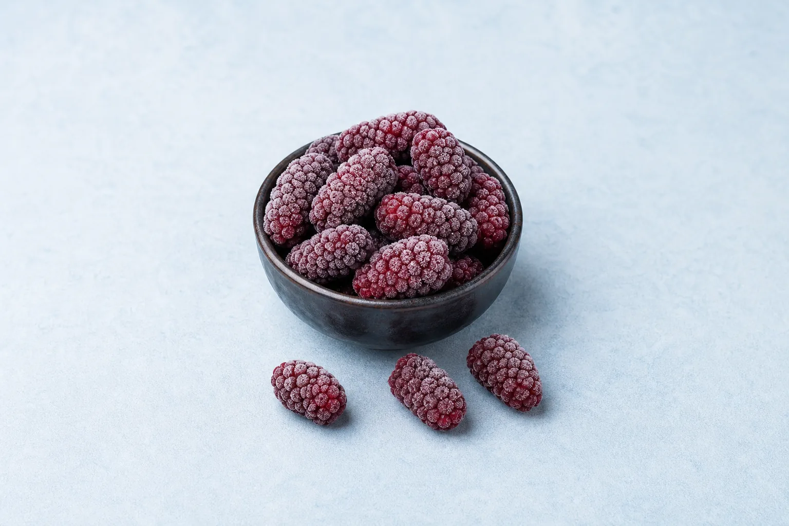 Deep-red frozen loganberries with a light frost in a small bowl.