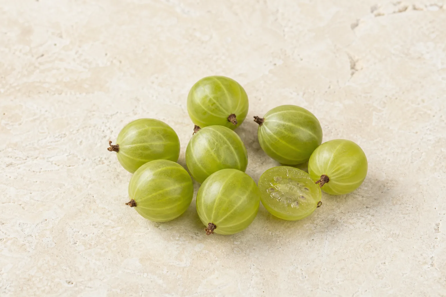 Fresh green gooseberries with translucent veined skin and one cut half showing pale seeded flesh.