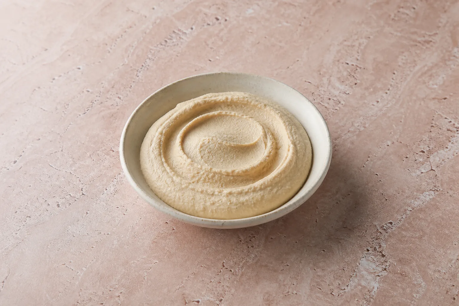 A shallow bowl of smooth plain beige hummus.