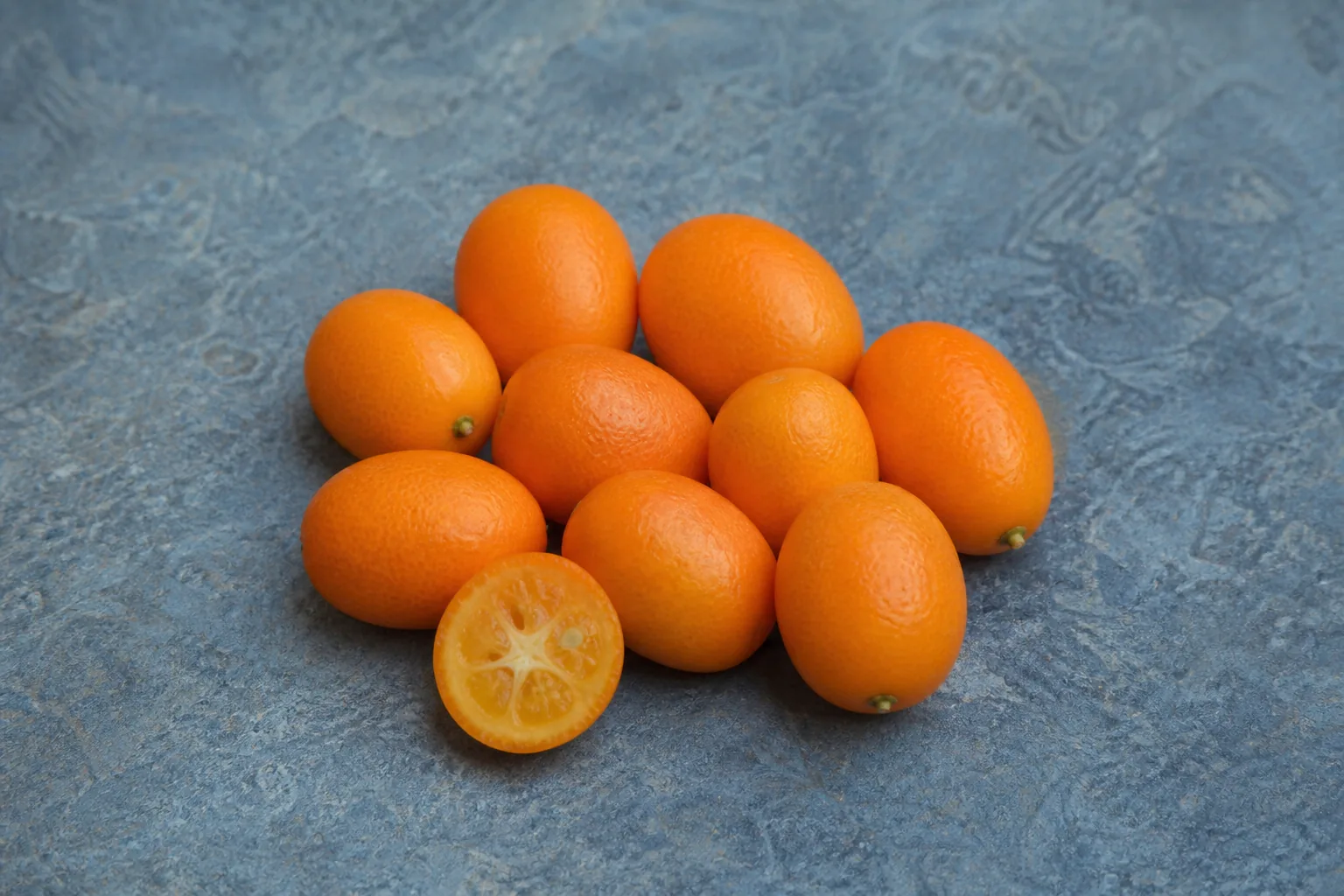 Small oval orange kumquats with one cross-cut half showing tiny citrus segments.