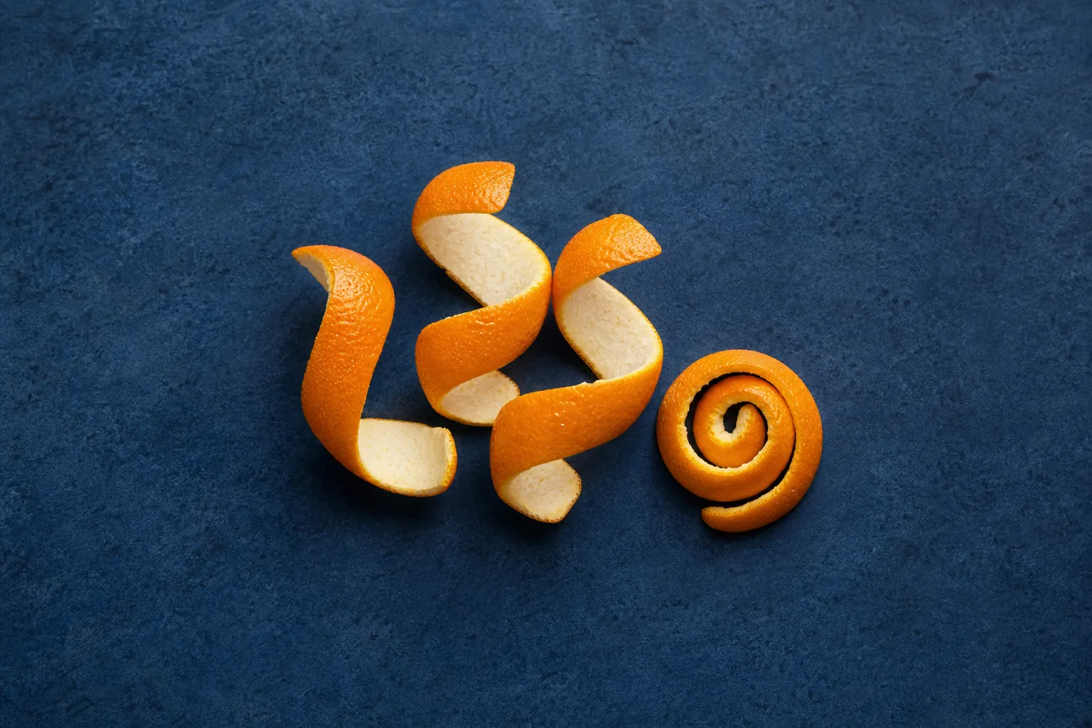 Fresh orange-peel strips and a curled spiral showing orange skin and thick white pith.