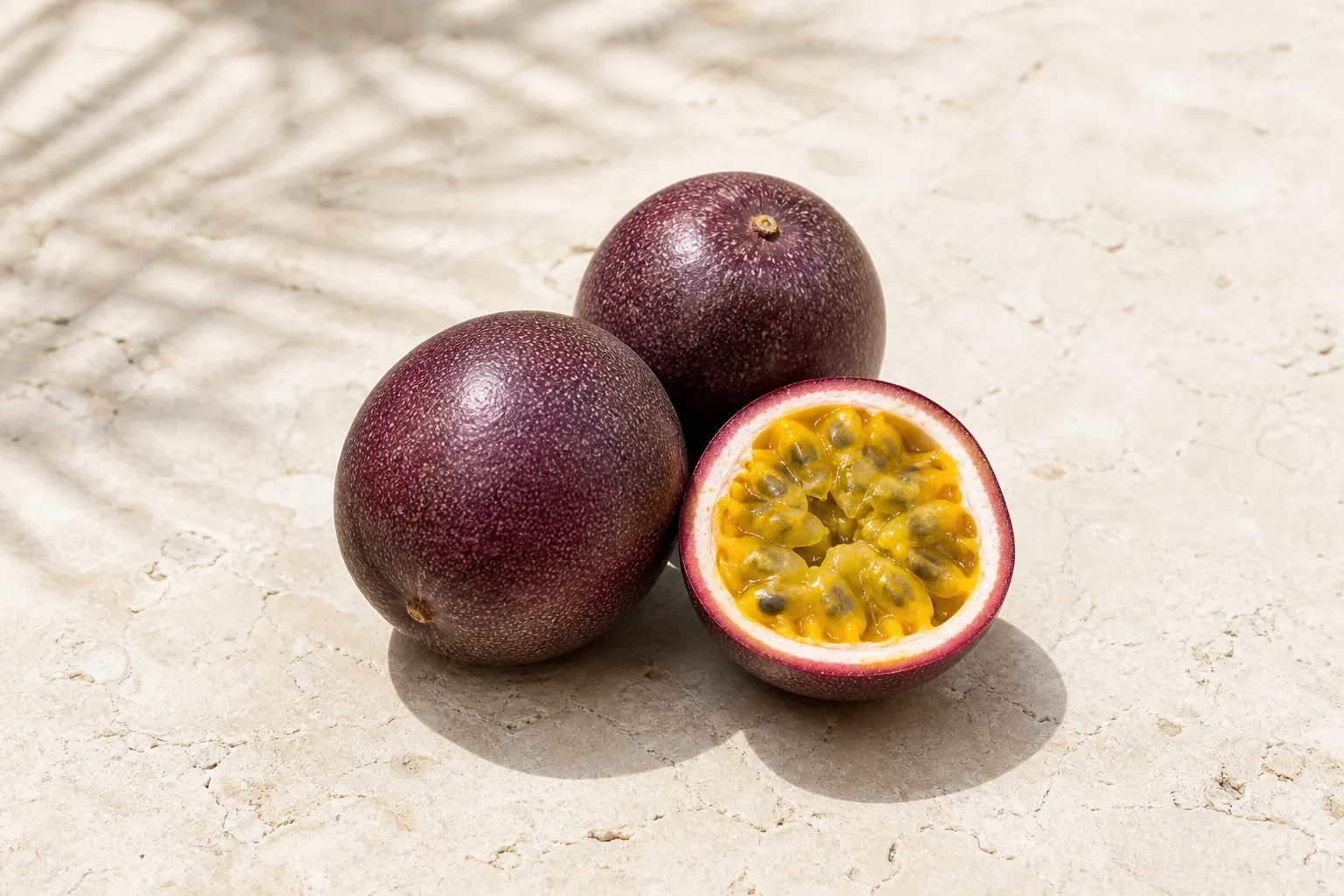 Two whole purple passion fruits and one cut half showing golden pulp and black seeds.