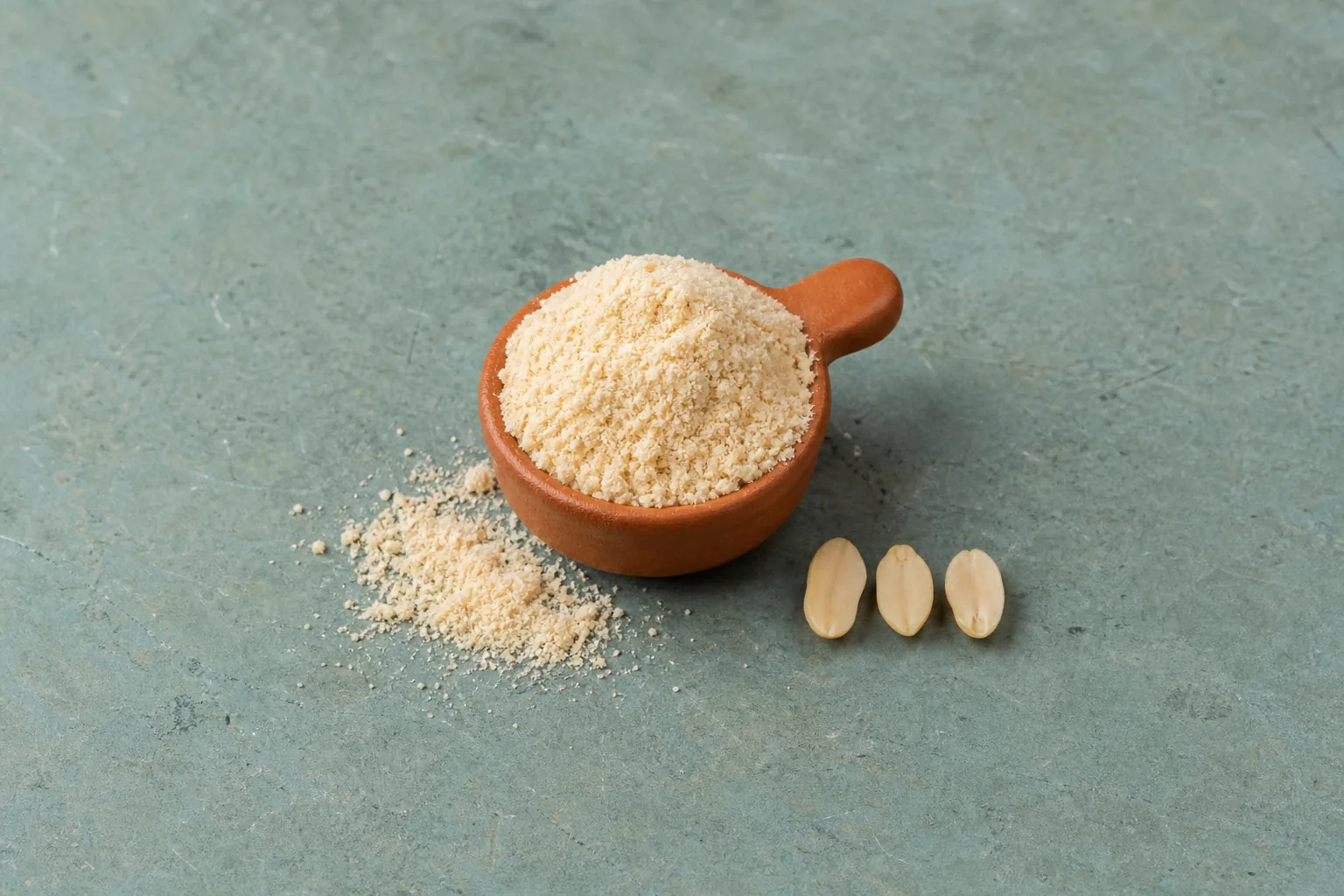 A terracotta cup of fine beige flour with a short spill and three peanut halves.