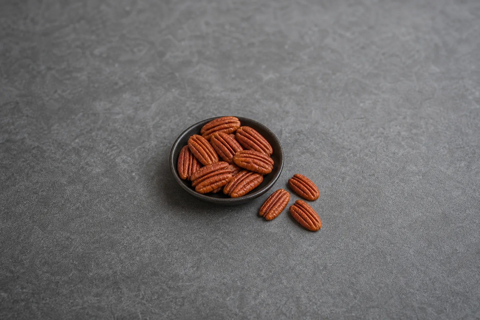 Raw pecan halves with elongated tapered shapes and tight lengthwise grooves in a small dark dish.