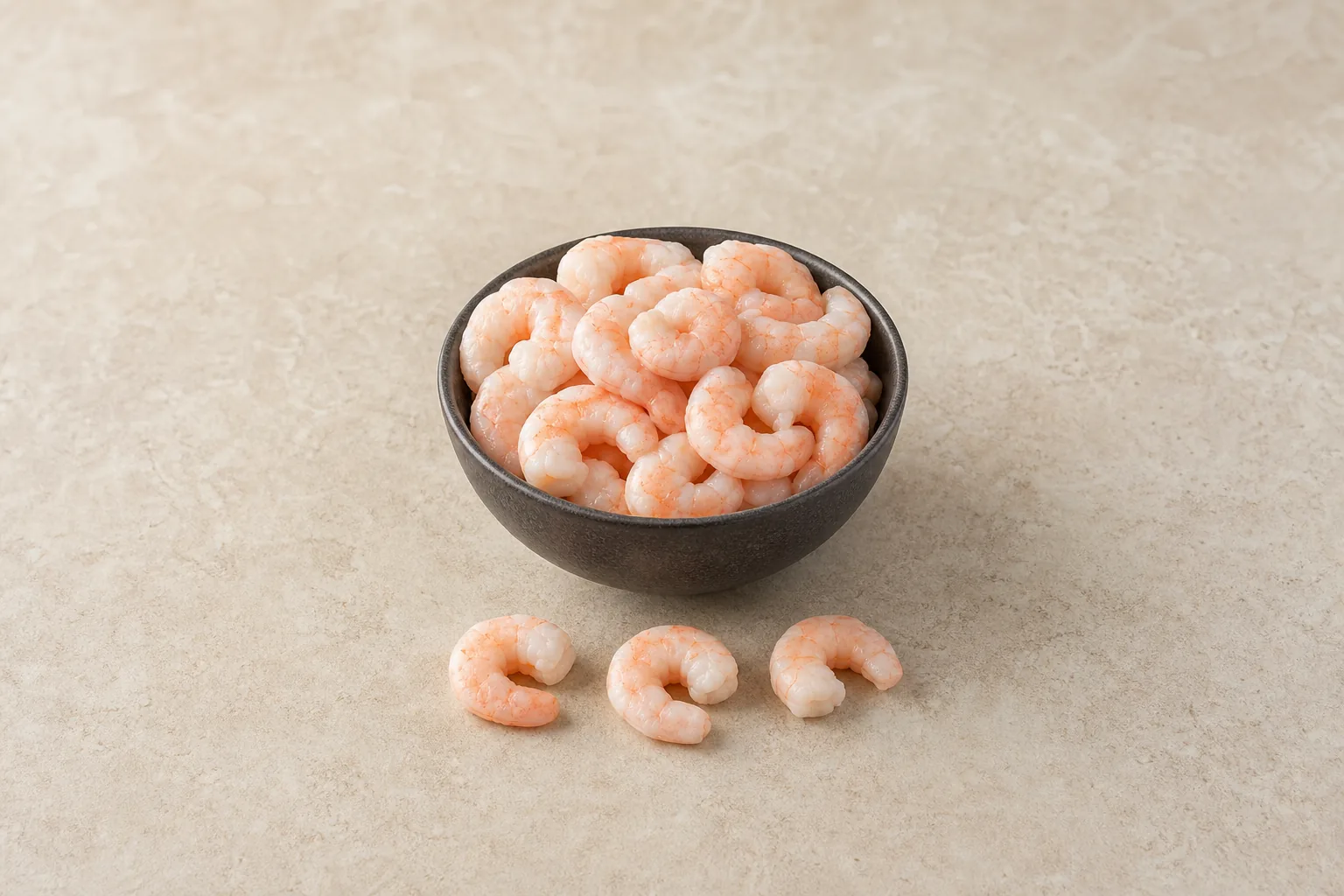 A small bowl of plain cooked peeled shrimp with several pink-white shrimp beside it.