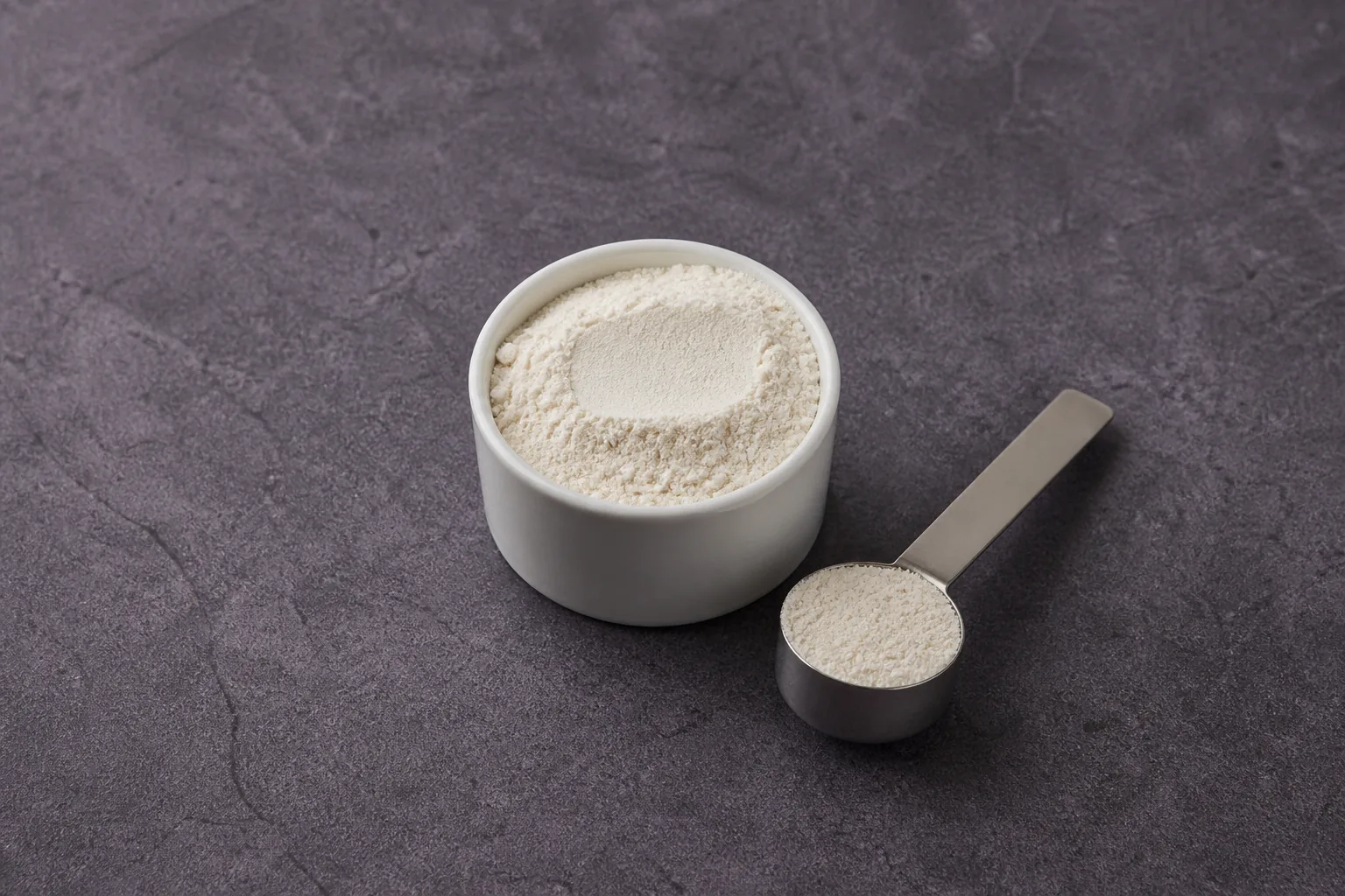 A white cup and short metal scoop holding very fine nearly white powder.