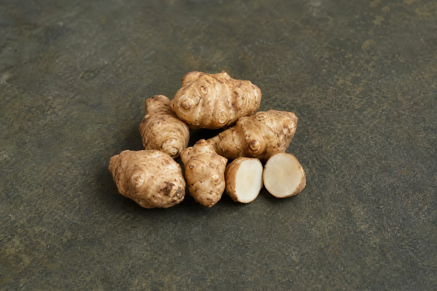 Knobby tan raw Jerusalem artichokes with one cut open to show ivory flesh.