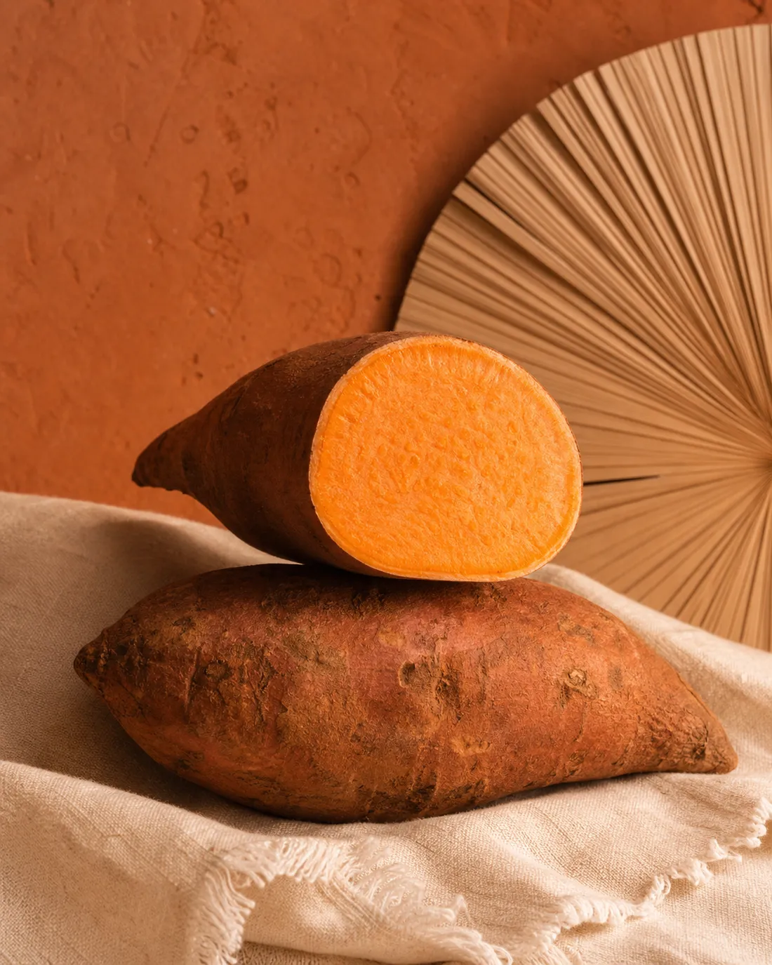 A whole and cut sweet potato on warm terracotta in golden tropical light.