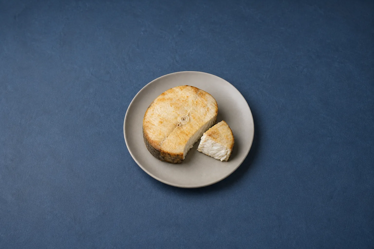 A thick cooked fish steak with a lightly browned surface and a cut section showing firm opaque flakes.