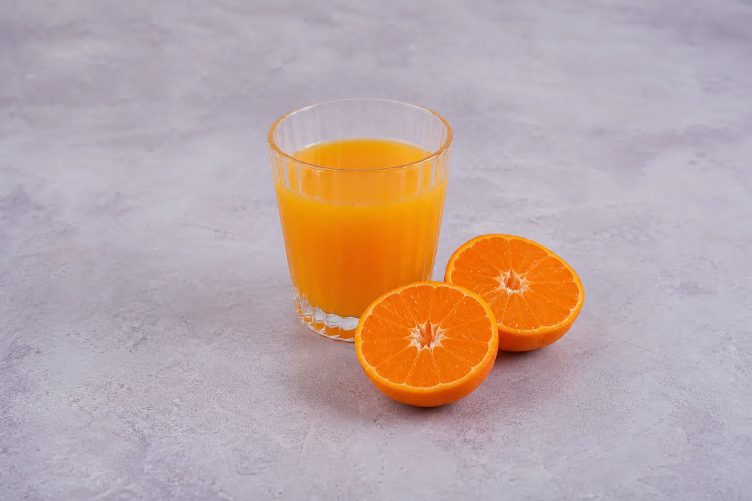 A glass of bright orange juice beside two tangerine halves.