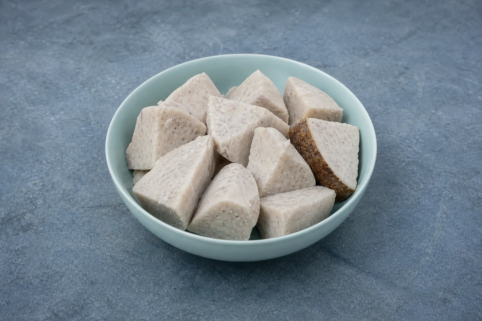 A shallow bowl of plain cooked off-white taro chunks with subtle lilac-grey speckles and one narrow skin-on edge.