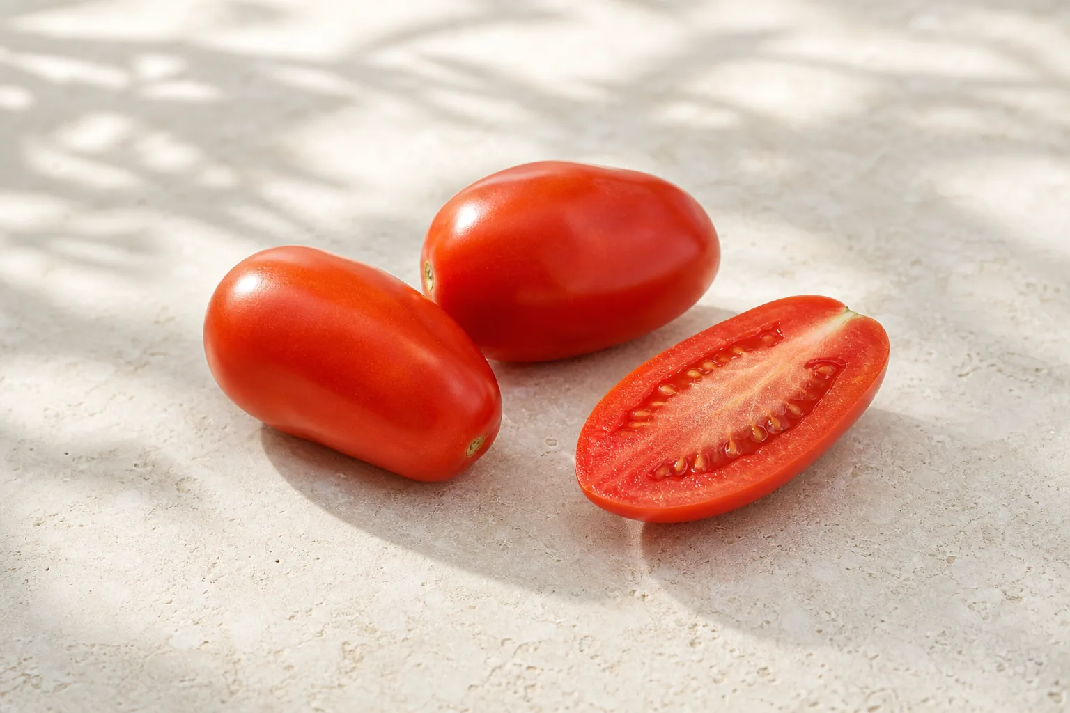 Whole raw Roma tomatoes and one lengthwise-cut half on pale limestone.