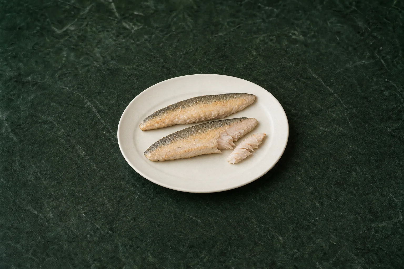 Two thin cooked skin-on fish fillets with pale flaky flesh and speckled silver-grey skin.