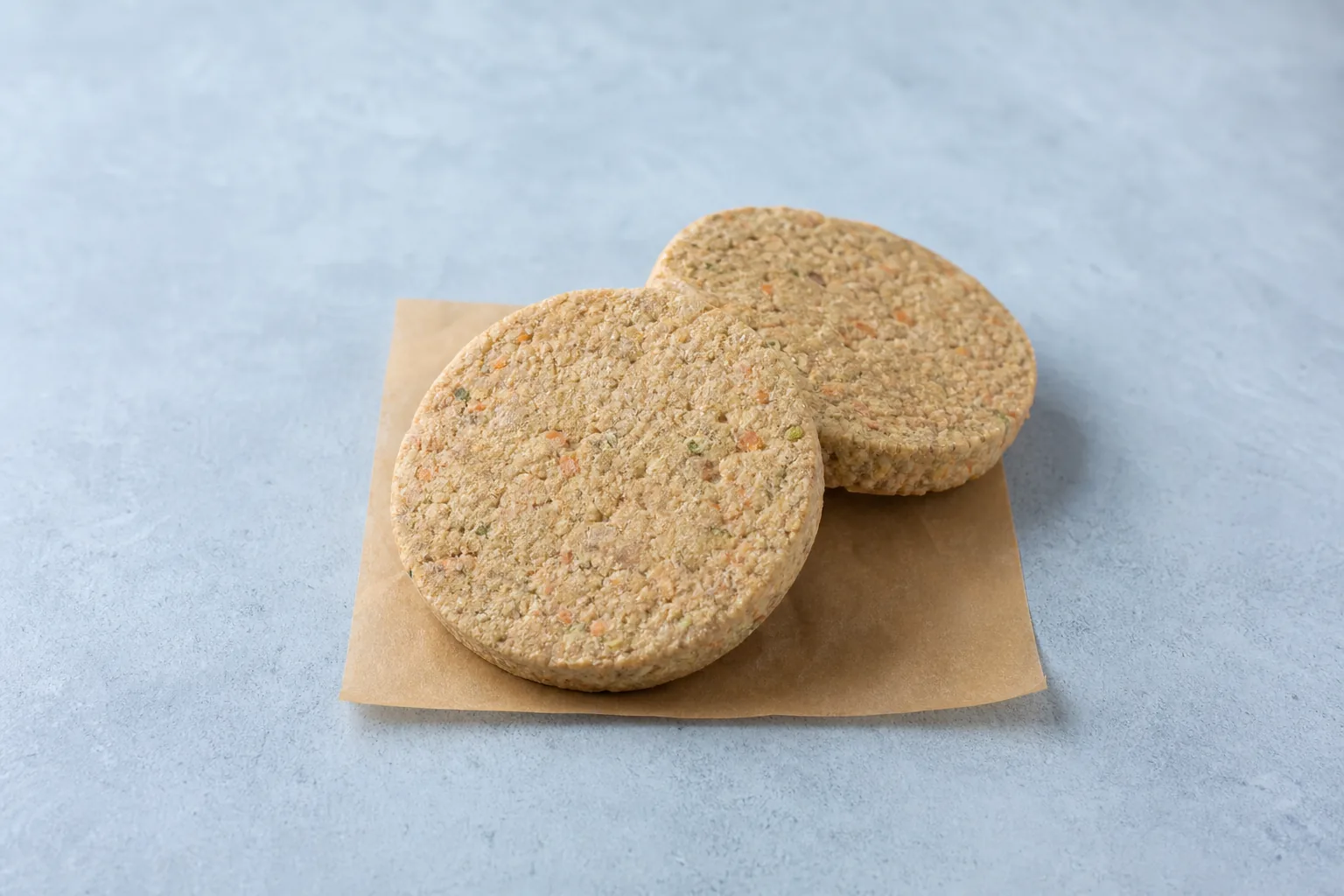 Two unprepared round vegetable burger patties on parchment with visible vegetable flecks.