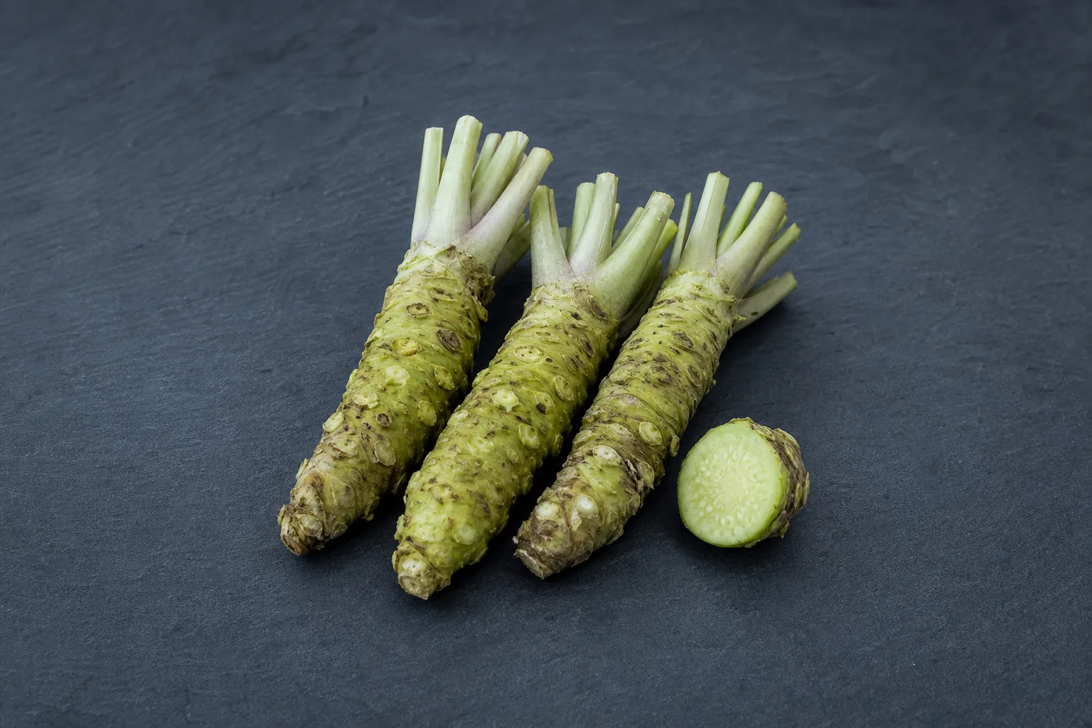 Knobbly pale-green raw wasabi rhizomes with a cut section showing pale-green flesh.