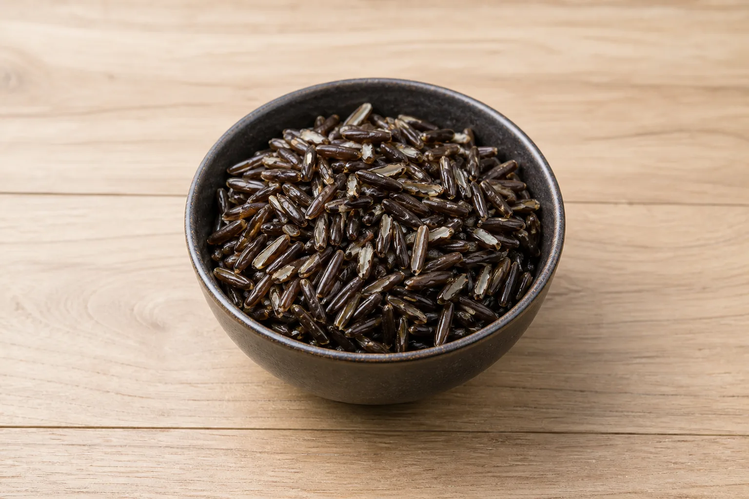 A bowl of plain cooked wild rice with long dark grains split to reveal pale interiors.