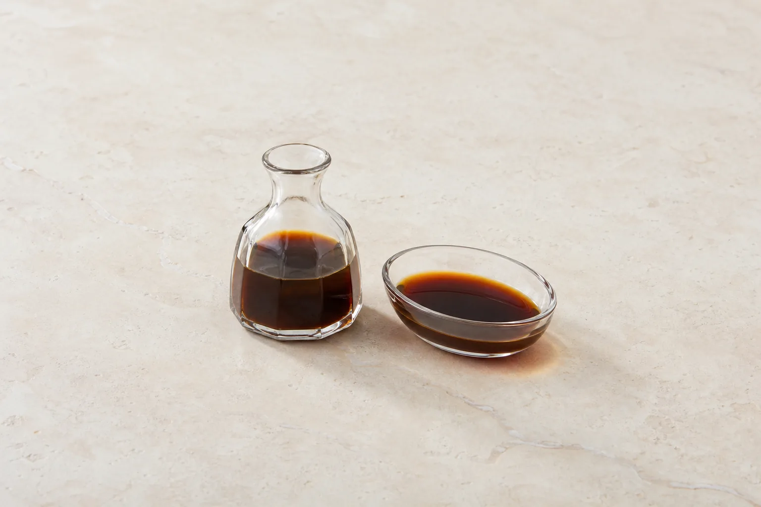 A clear cruet and small dish of thin dark reddish-brown sauce.