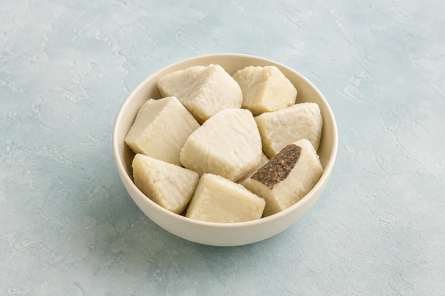 A small bowl of plain cooked white-fleshed yam pieces, including one piece with rough brown skin attached.